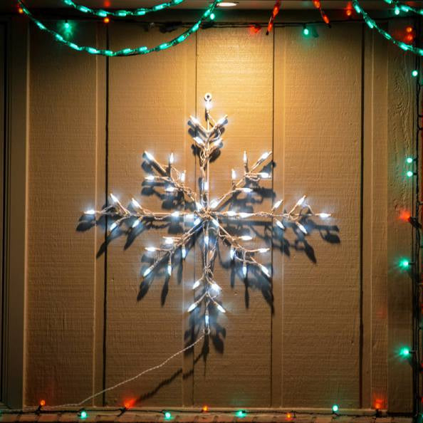30-inch Classic Branch Snowflake LED Display glowing white mounted against a house lit at night surrounded by red and green string lights