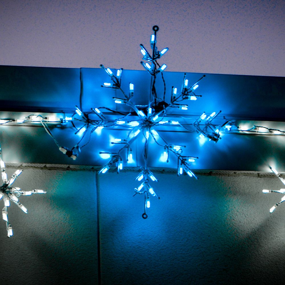 Classic Branch Snowflake Light Display with illuminated ice blue LEDs mounted along a building facade, with white lights nearby