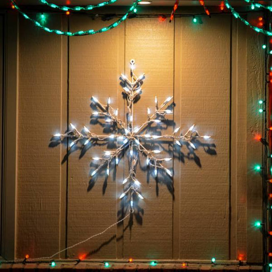 30-inch Classic Branch Snowflake LED Display glowing white mounted against a house lit at night surrounded by red and green string lights
